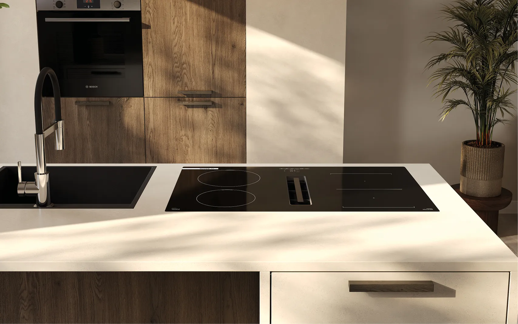 Detailansicht Kochinsel: Induktionskochfeld mit integriertem Abzug, helle Arbeitsplatte, links schwarze Einbauspüle mit Chromarmatur; dahinter Hochschrankwand in Holz und Beige mit Bosch-Backofen; rechts Topfpflanze.